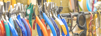 Jewelry pliers with different color handles are lined up and hanging on a rod and a pair of sunglasses can be seen hanging behind them