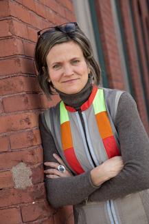 Laura Burkett, director of Metalwerx, smiles at the camera leaning against a red brick wall.