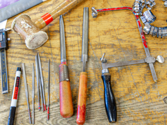 Jewelry tools on a workbench including files, a sawblade, a mallet, and more