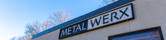 Outside view of a tan building with a large sign that says Metalwerx
